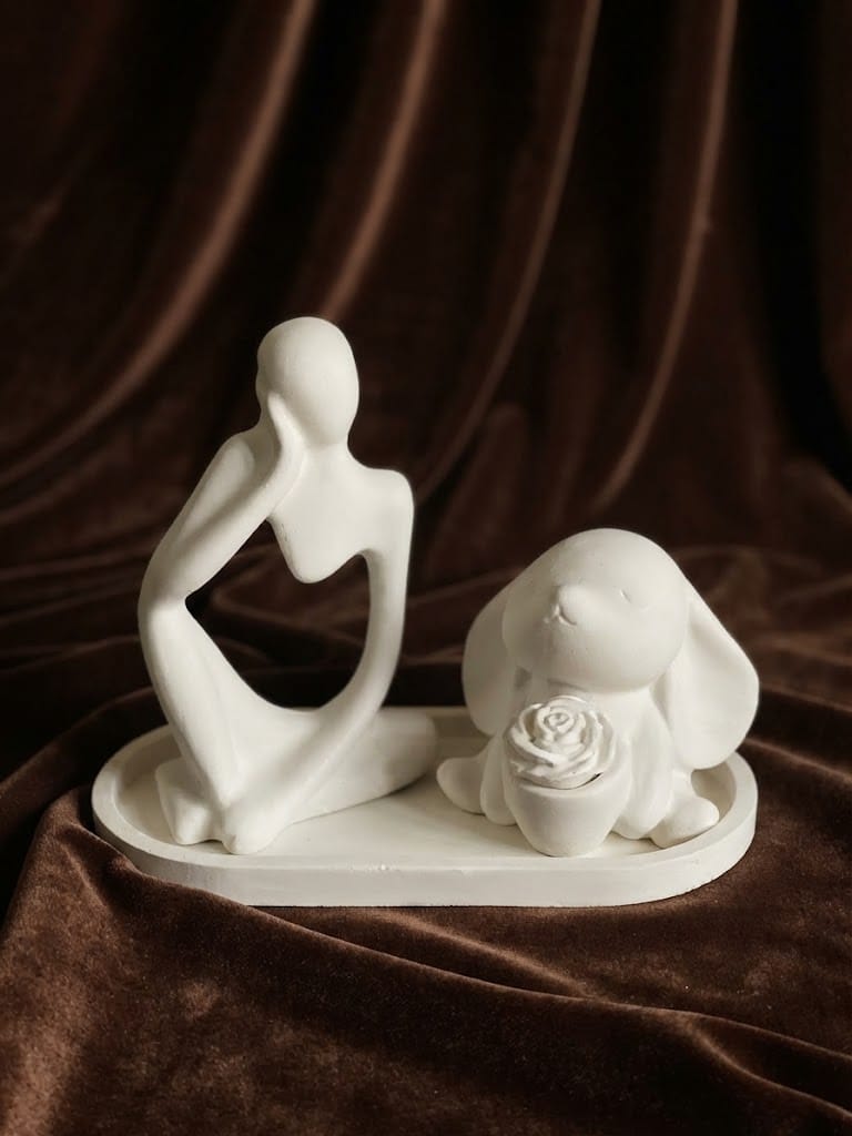 Sculptural couple figurine and floral accent arranged on an ivory tray against dark brown drapery