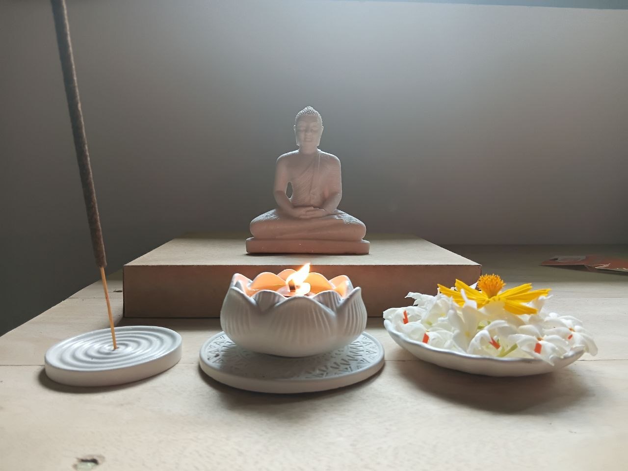 A meditative still life with a seated figure, incense holder, petal burner and flowers
